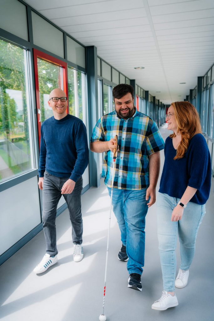 Drei Personen in natürlicher Umgebung mit freundlichem Blick, fotografiert für eine Recruiting-Kampagne.